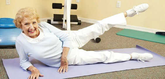 Пожилая женщина делает гимнастику на коврике